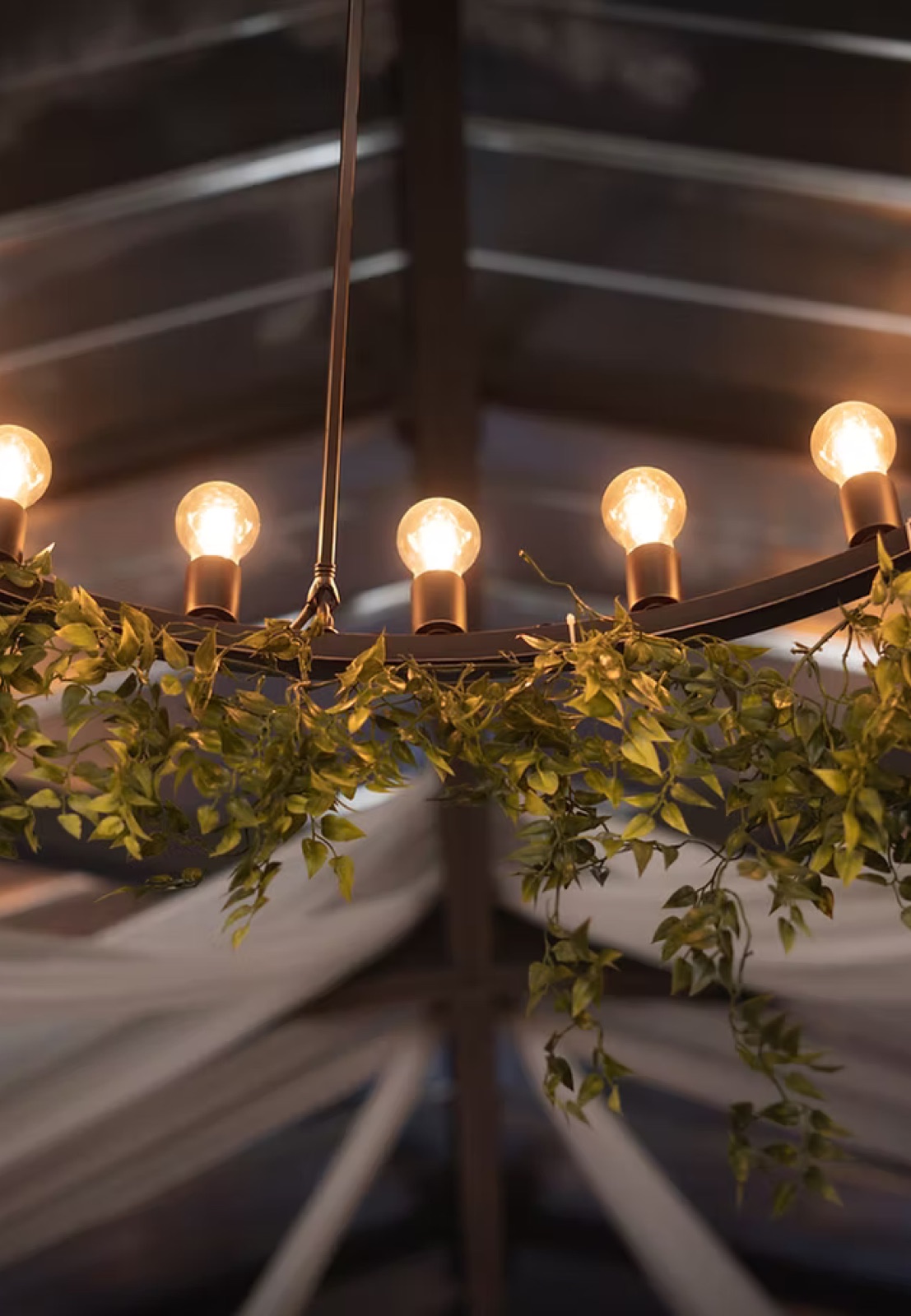 A greenery-wrapped chandelier glowing above a reception tent